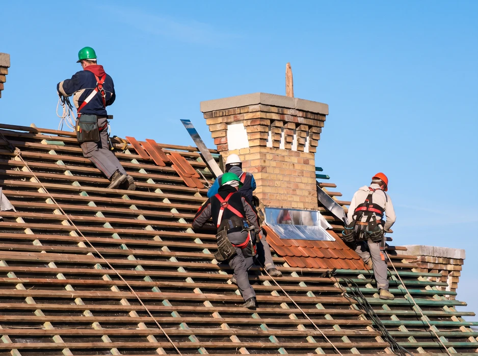 Quatre couvreurs en harnais de sécurité travaillent sur une toiture en cours de réfection