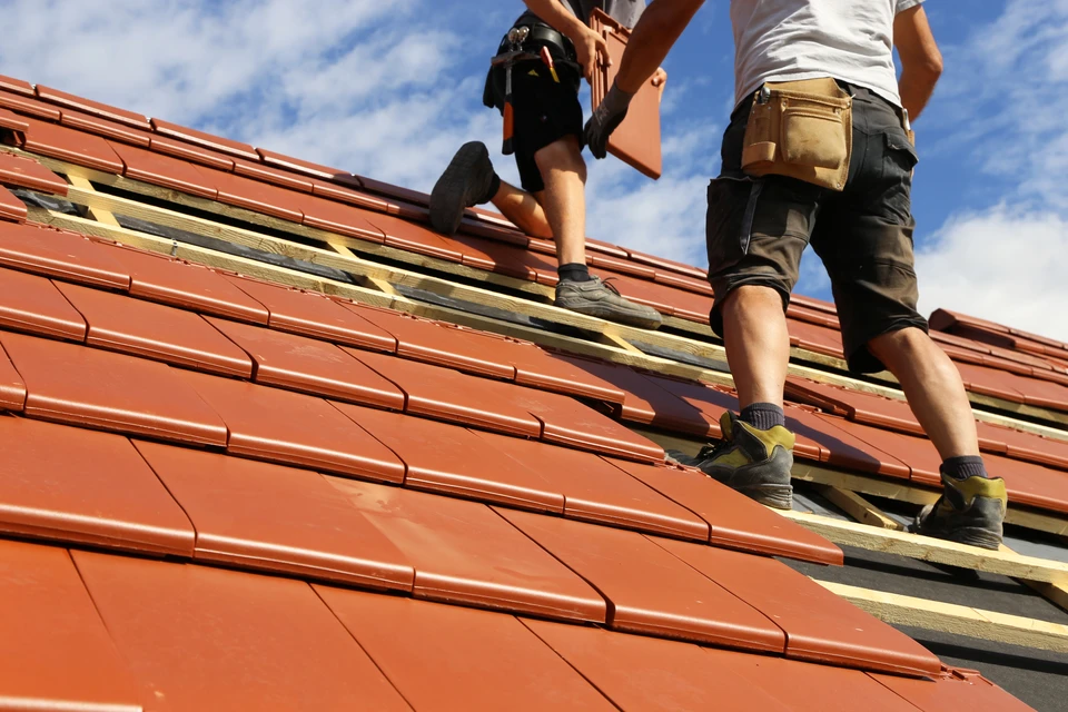 Couvreur en tenue de travail grise posant des tuiles métalliques noires brillantes sur une toiture en cours d'installation