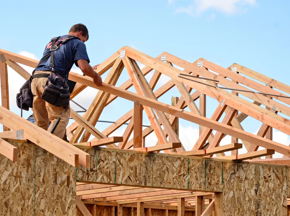 Charpentier en hauteur sur ossature bois d'une maison en construction, manipulant des fermes de toit triangulées